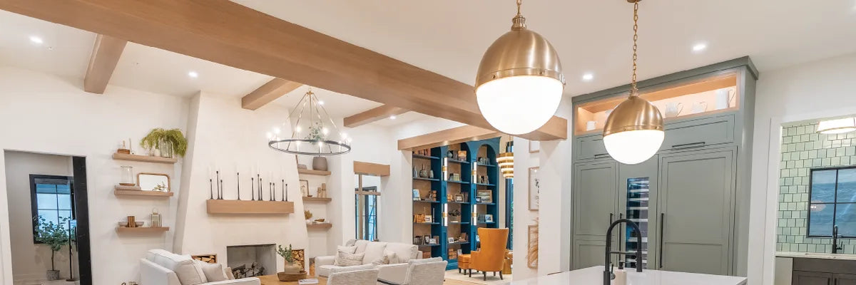 Open concept living space with white walls, exposed wooden ceiling beams, modern brass and glass pendant lights, and a mix of contemporary and rustic furniture.