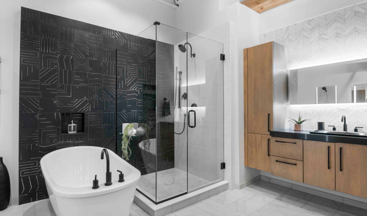 Spacious modern bathroom featuring a freestanding tub with black fixtures, a glass-enclosed shower with dark tile wall, and wood cabinetry with a backlit mirror.
