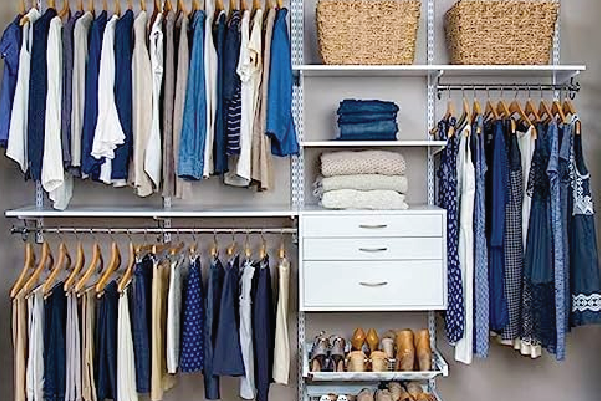Closet organization system with hanging clothes on wooden hangers, folded sweaters on shelves, woven baskets on upper shelves, and shoes neatly arranged below.