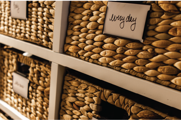 Woven storage baskets with handwritten label cards placed on white shelving, captured in warm natural lighting.