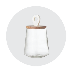 Clear glass storage jar with a rounded shape and a wooden lid featuring a white ceramic handle on top against a light neutral background.
