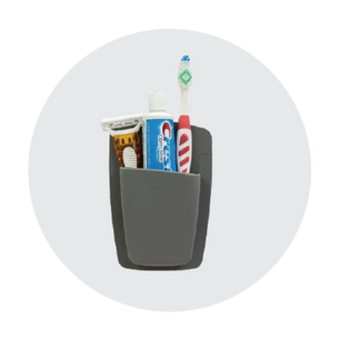 Compact dark gray wall-mounted organizer holding a toothbrush, toothpaste, razor, and small hairbrush against a light gray circular background.