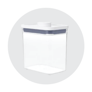Transparent rectangular food storage container with a white lid and gray sealing ring, shown against a light gray circular background.