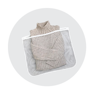Folded beige knitted sweater placed inside a white mesh laundry wash bag on a soft gray circular background.