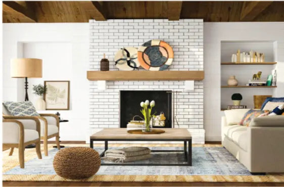 Bright living room featuring a white brick fireplace with wooden mantel, neutral-toned seating, decorative shelving, and a woven floor pouf on a patterned rug.