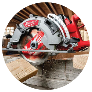 Red and silver circular saw actively cutting through stacked wooden planks inside a construction site with visible timber framing.