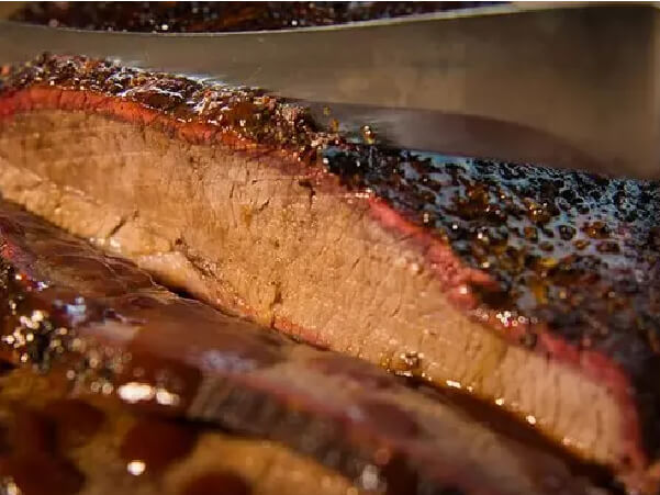 Close-up of a smoked brisket slice showing a dark seasoned crust with a visible smoke ring and tender, juicy interior.