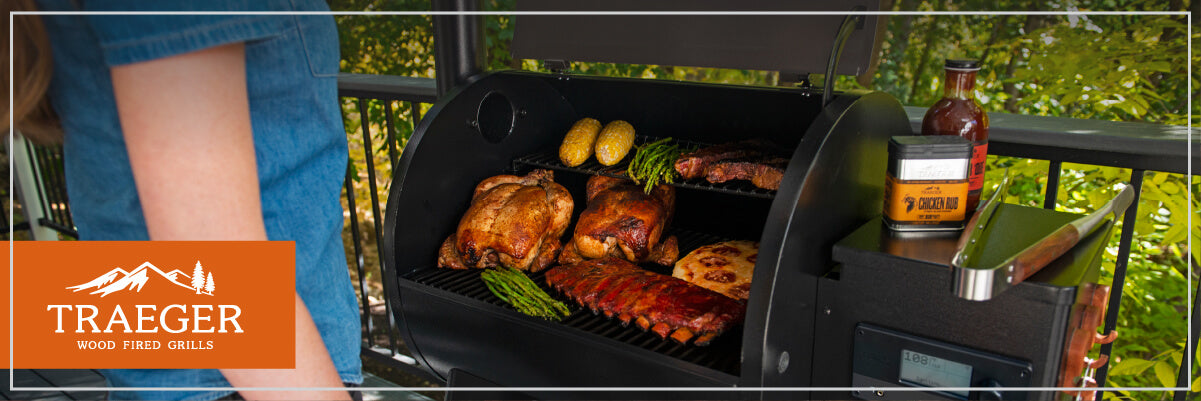Outdoor wood-fired grill open to reveal various meats and vegetables cooking, with a person tending to the food nearby on a deck railing.