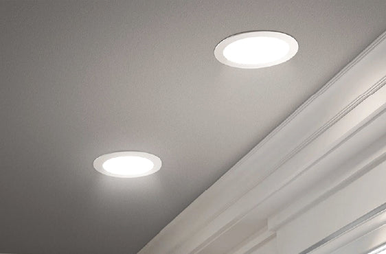 Two round recessed ceiling lights emitting bright white light installed in a smooth gray ceiling above decorative white crown molding.